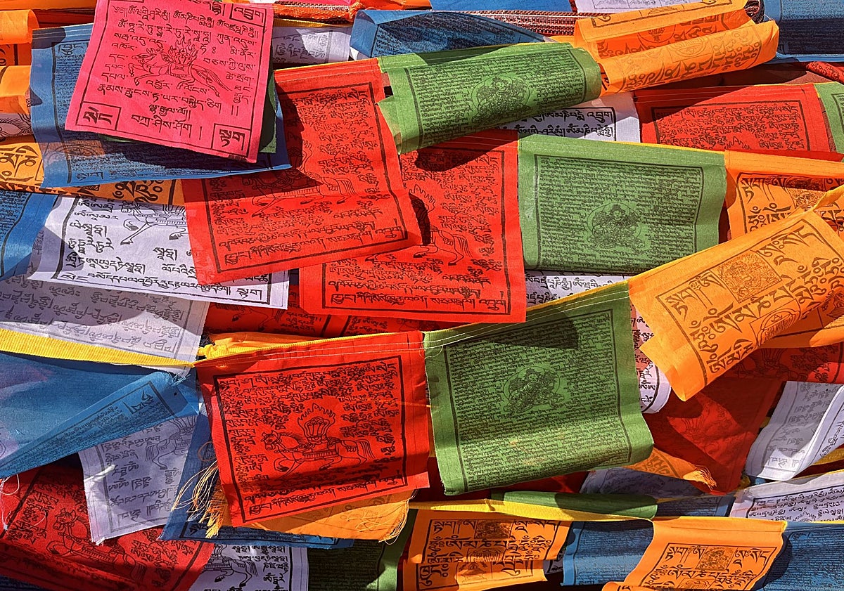 Imagen principal - Banderas de oración y una peregrina con su rosario y su móvil en el palacio-castillo de Yumbulakang o Yumbu Lha Khang, el primer edificio construido en Tíbet según la tradición budista.