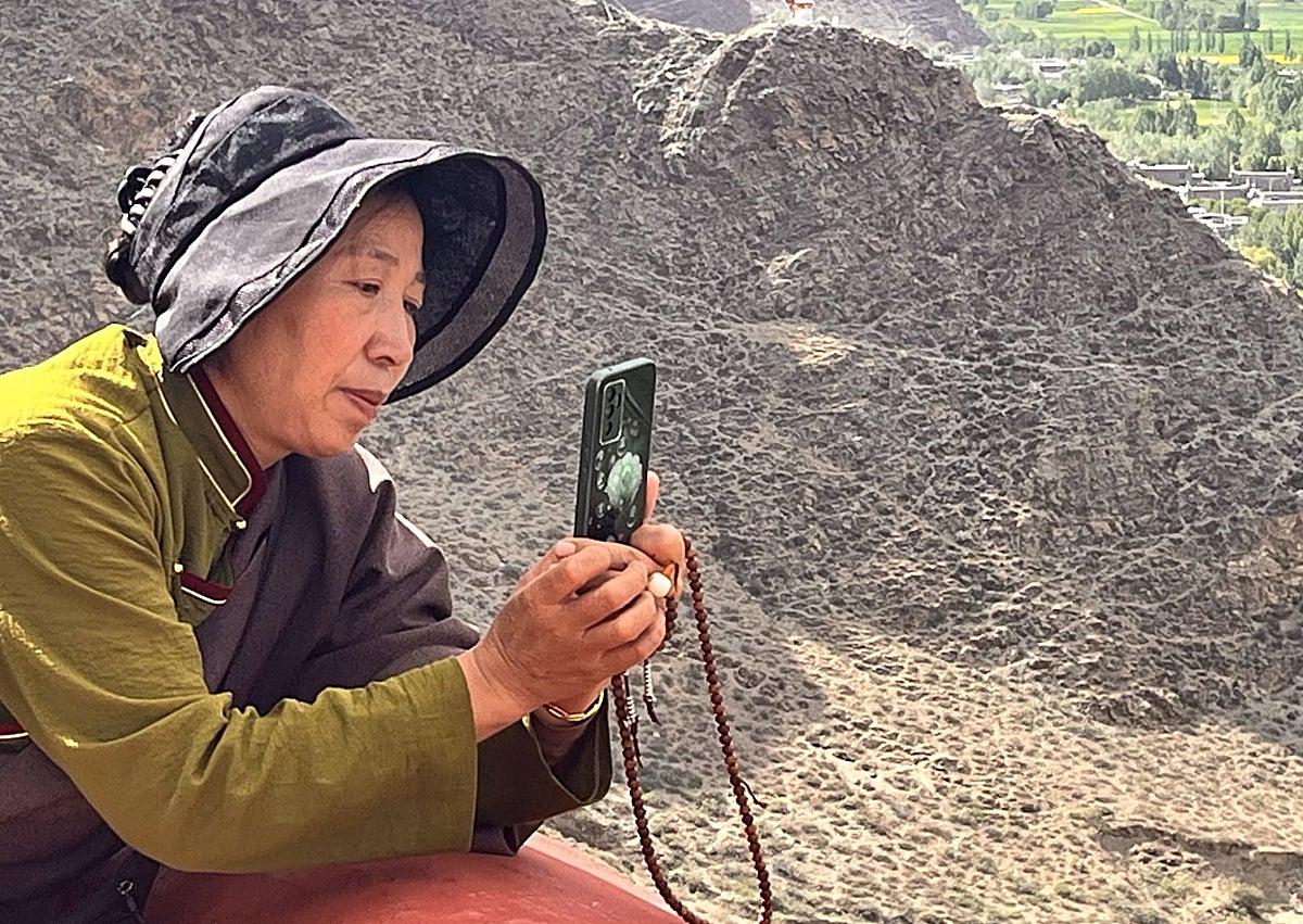 Imagen secundaria 1 - Banderas de oración y una peregrina con su rosario y su móvil en el palacio-castillo de Yumbulakang o Yumbu Lha Khang, el primer edificio construido en Tíbet según la tradición budista.