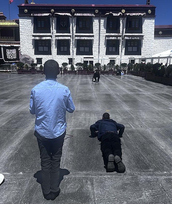 Imagen secundaria 2 - Una joven influencer posa ante unos molinillos de oración en las inmediaciones de Jokhang. Una mujer con su hijo a la espalada en la plaza Dhurbar, en el e barrio de Barkhor. Peregrinos postrados y orando ante la fachada del sagrado complejo de Jokhang.