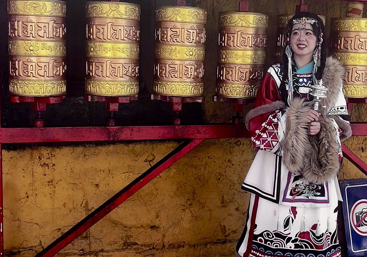 Imagen principal - Una joven influencer posa ante unos molinillos de oración en las inmediaciones de Jokhang. Una mujer con su hijo a la espalada en la plaza Dhurbar, en el e barrio de Barkhor. Peregrinos postrados y orando ante la fachada del sagrado complejo de Jokhang.