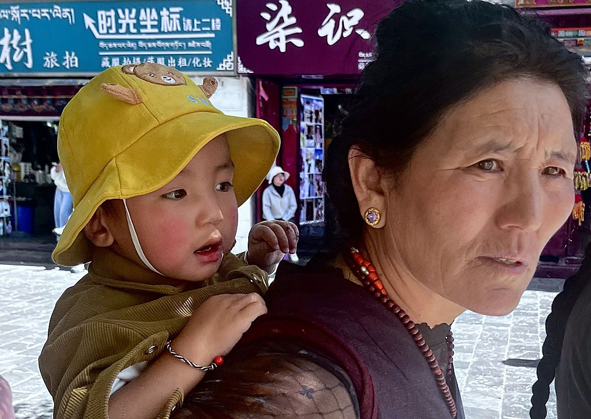 Imagen secundaria 1 - Una joven influencer posa ante unos molinillos de oración en las inmediaciones de Jokhang. Una mujer con su hijo a la espalada en la plaza Dhurbar, en el e barrio de Barkhor. Peregrinos postrados y orando ante la fachada del sagrado complejo de Jokhang.