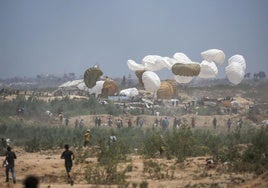 Decenas de palestinos corren hacia el lugar donde aterrizan paquetes de ayuda humanitaria en paracaídas en el centro de Gaza.