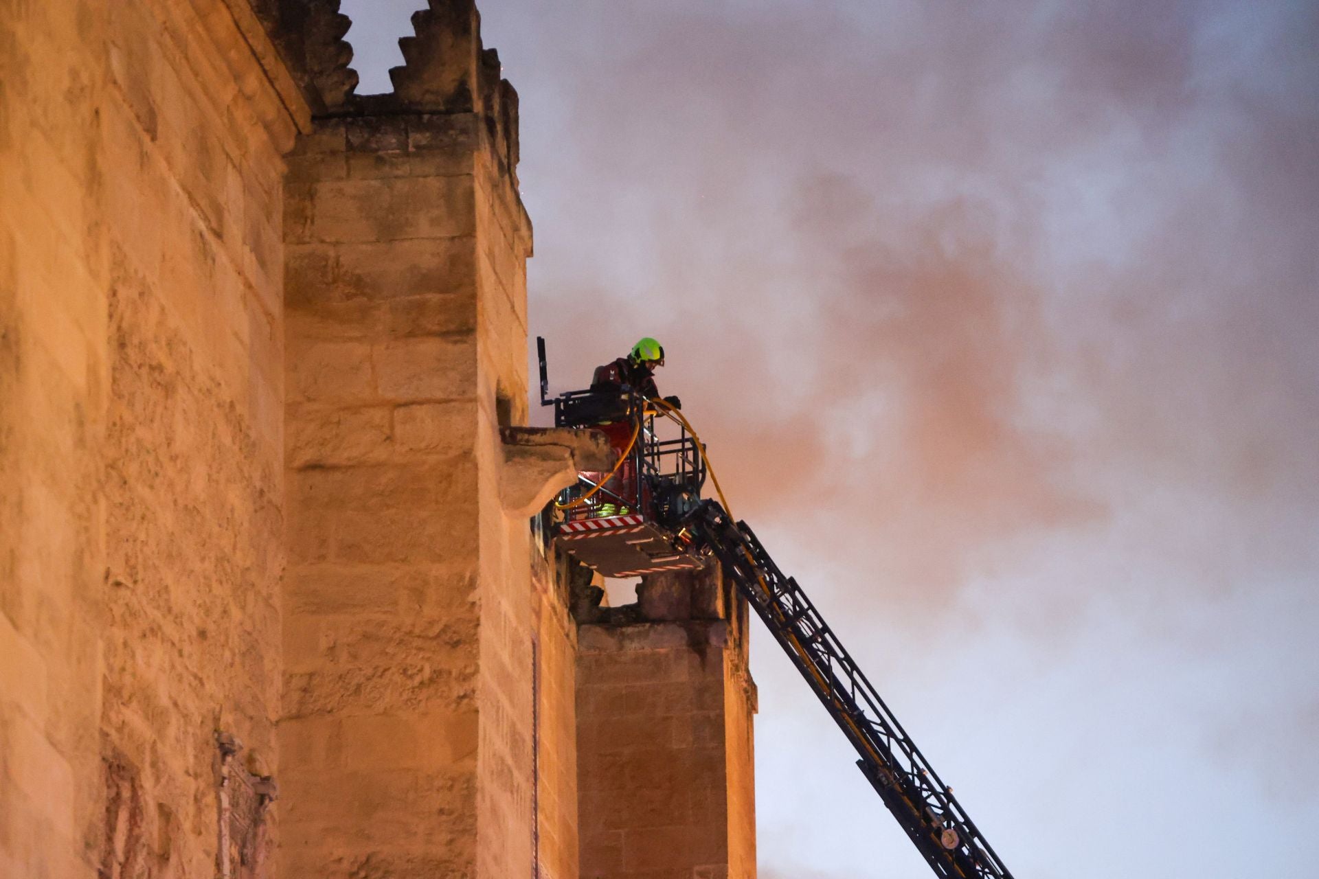 Imagen principal - En la imagen superior, un bombero que participaba en las tareas de extinción desde una escala exterior; debajo, aceso al interior de la Mezquita-Catedral de Córdoba por parte de los servicios de emergencias; por último, las llamas y un denso humo negro fueron la señal de alarma para que varios vecinos alertasen a las autoridades del incendio desatado este viernes.