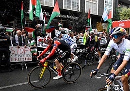 Los ciclistas pasan por delante de algunos manifestantes.