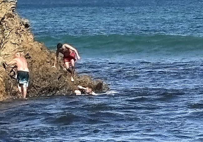 A la derecha, Joaquín inmóvil agarrado a la roca, mientras José llega con su mujer y otro joven de bañador rojo les ayuda a subir.