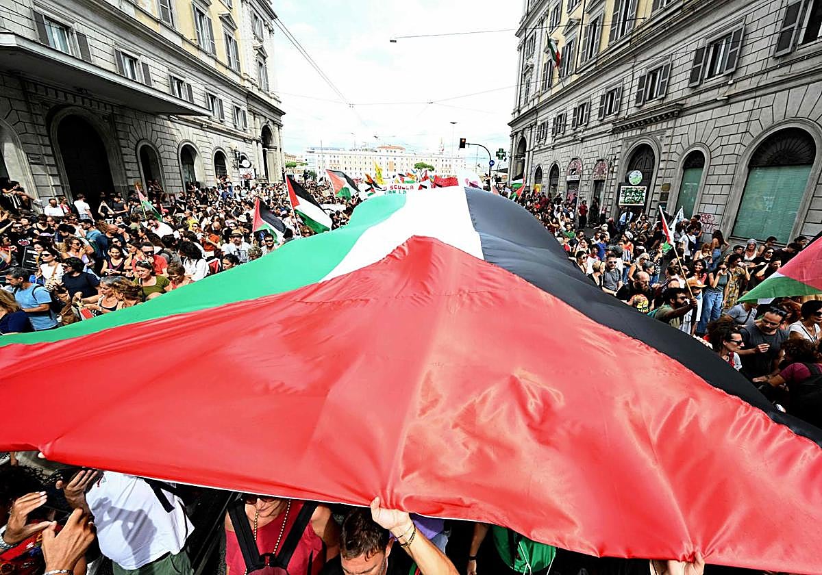 Cientos de manifestantes ondean una bandera palestia gigante por una calle de Roma.