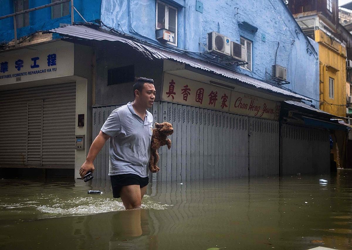 Imagen secundaria 1 - Un hombre sostiene a su perro mientras camina por una calle de Macao; sacos de arena se apilan frente a un restaurante en Hong Kong y el lodo cubre una céntrica arteria de Hualien (Taiwán).