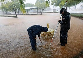 Unos operarios facilitan el drenaje del agua a través de una alcantarilla en Almussafes.