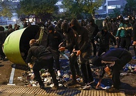 Jóvenes encapuchados recogen botellas de un cubo de basura.