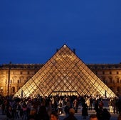 La gente camina cerca de la pirámide de cristal del museo del Louvre.