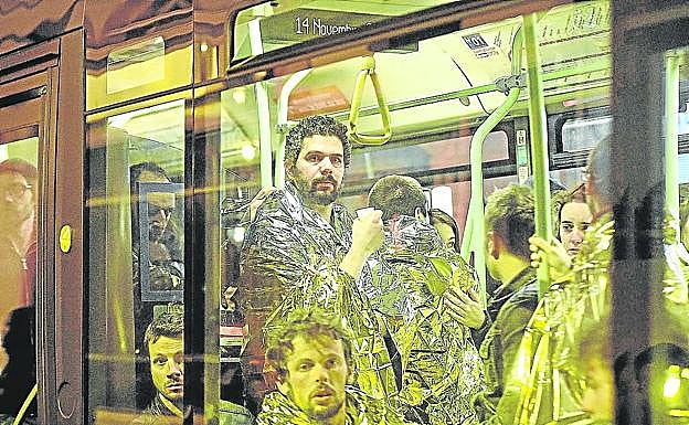 Personas cubiertas con mantas térmicas son evacuadas en un autobús del lugar de los hechos.