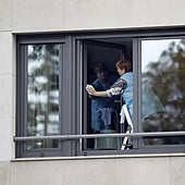 Una empleada del hogar trabaja limpiando una ventana.