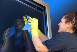 Una empleada de hogar, limpiando un cristal.