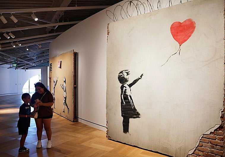 Imagen principal - Arriba, dos visitantes junto a un Bansky, debajo un fan de 'Star Wars' fotografía una de las maquetas y dos niñas, junto a un R2D2.