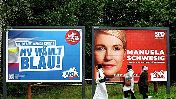 Tres mujeres pasan junto a dos carteles electorales en Pomerania.