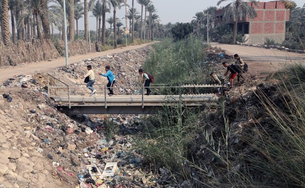 Un grupo de niños cruza un puente sobre un río lleno de basura en Egipto. 