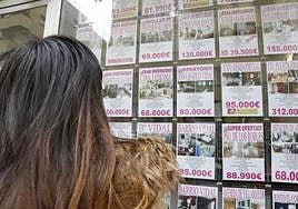 Una mujer observa el escaparte de una inmobiliaria lleno de ofertas de venta de viviendas.