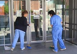 Dos mujeres limpiando en la puerta de un colegio.