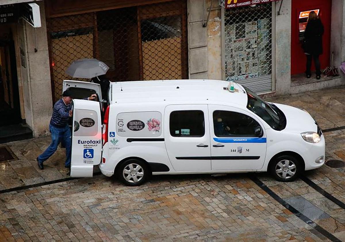 Un taxista ayuda a una persona con movilidad reducida a entrar en el vehículo.