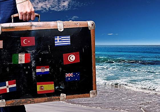 Una maleta de viaje con banderas de distintos países junto a la orilla del mar.