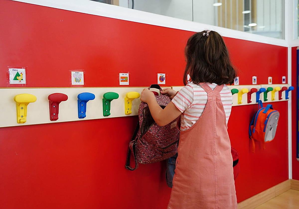 Una niña dejando la mochila en el perchero de la guardería.