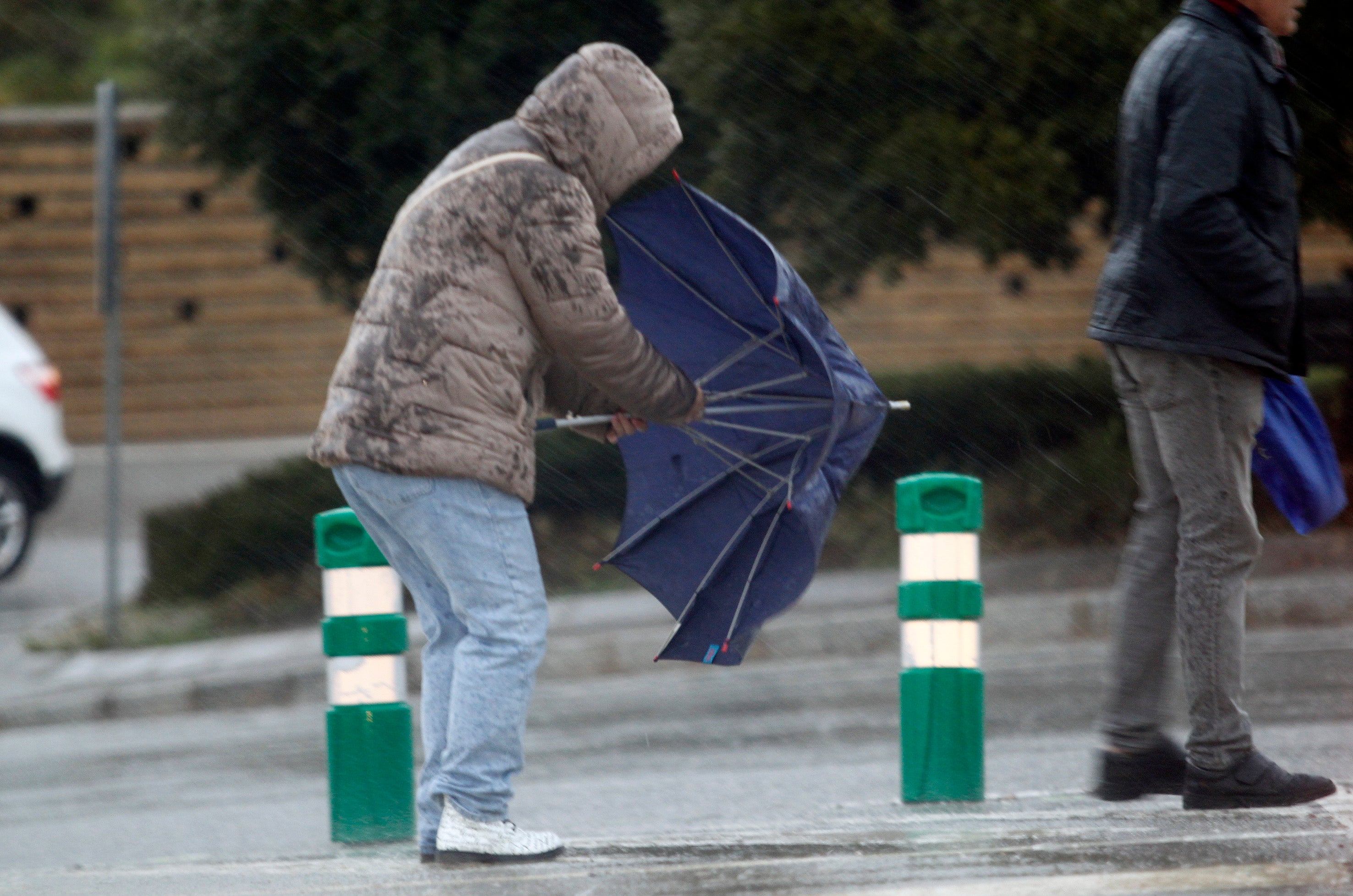 Un hombre trata de cerrar el paraguas pese al viento.