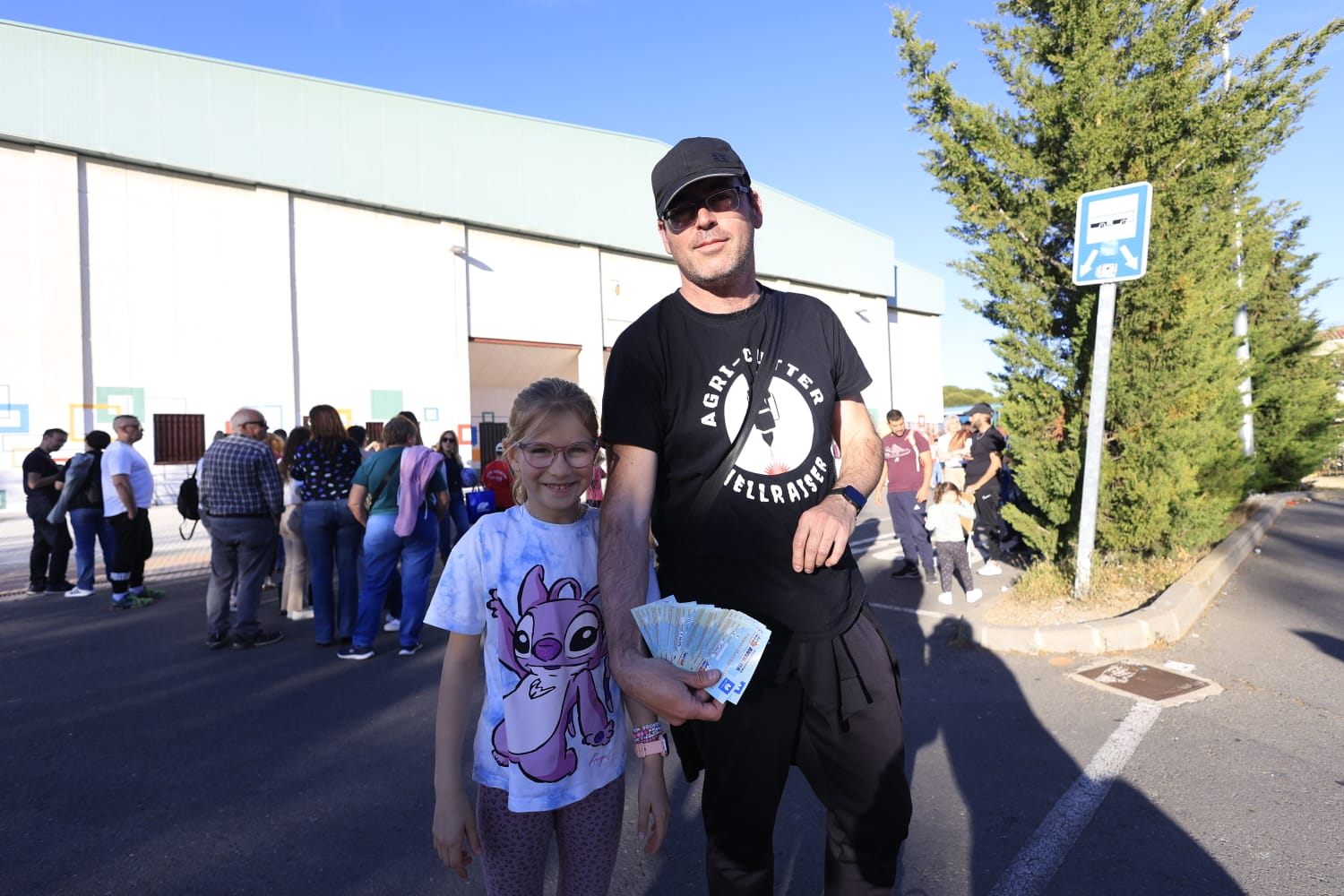 Un padre y su hija posan con varias entradas delante de la gran cola de aficionados que esperaban para comprar entradas para la final entre Avenida y el Valencia Basket.