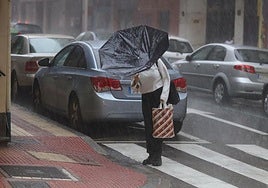 Una mujer trata de sujetar el paraguas a pesar del viento.