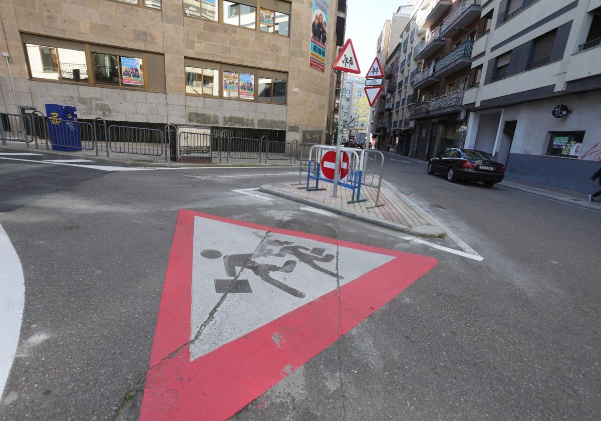 Una señal sobre la calzada y varias verticales de advertencia por proximidad a un colegio.