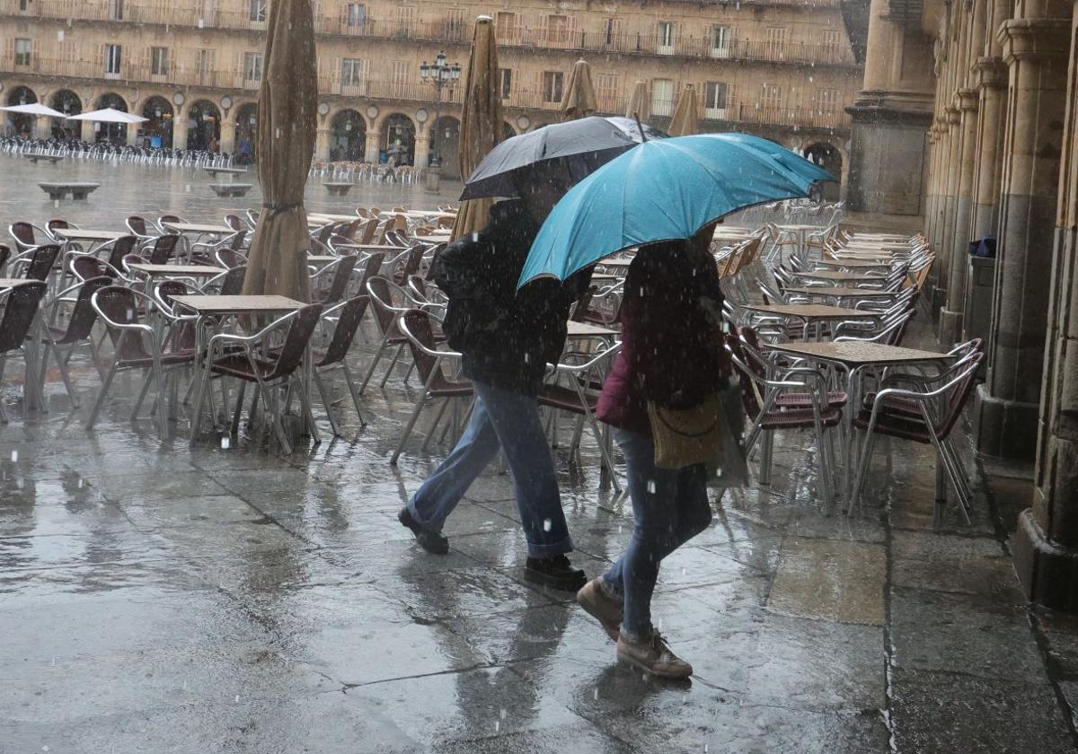 Dos personas pasean por la Plaza Mayor con sus paraguas un día de lluvia.
