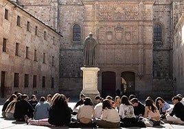 Estudiantes sentados frente a la fachada de la Universidad.