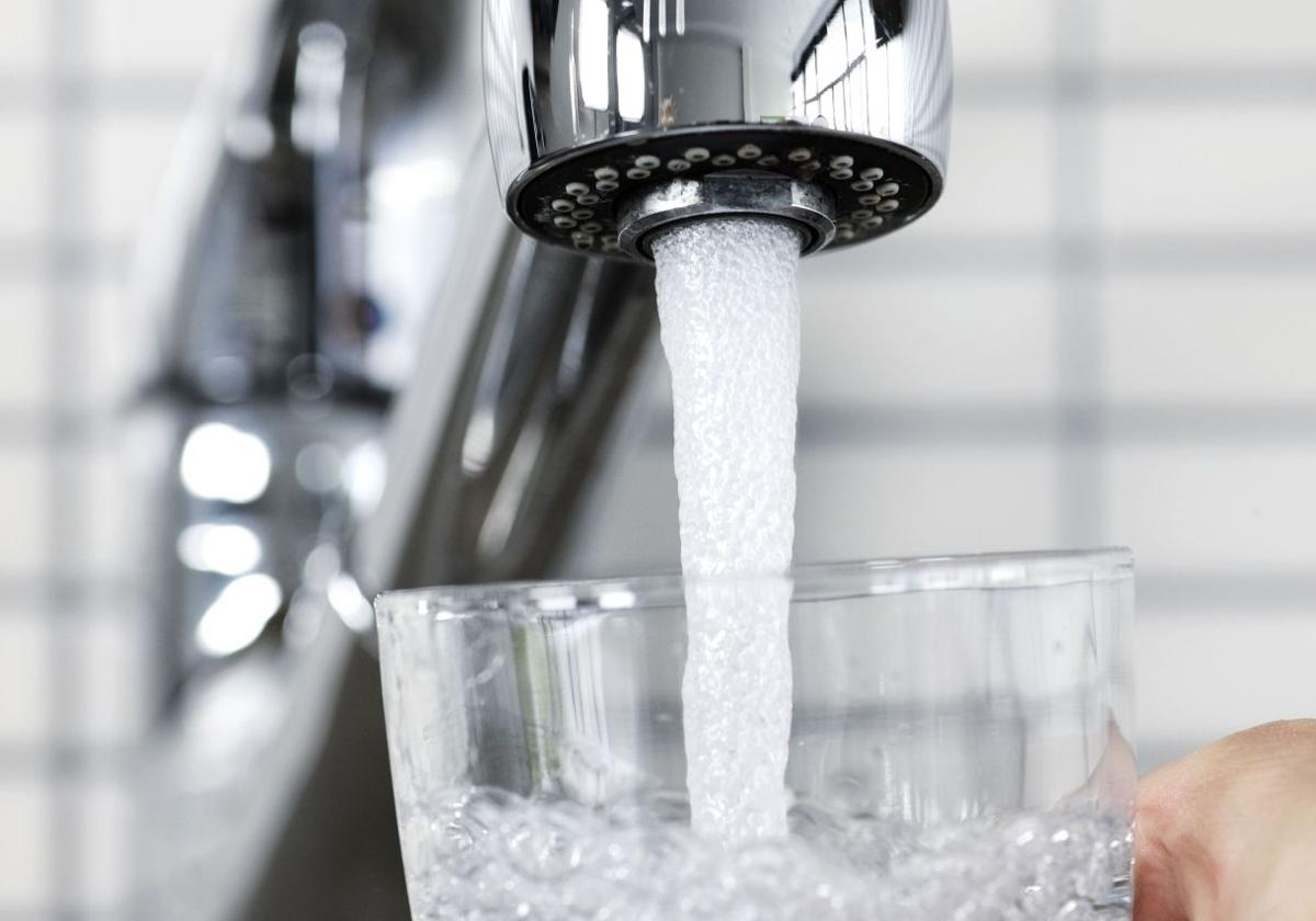 Una persona coge agua del grifo en un vaso.