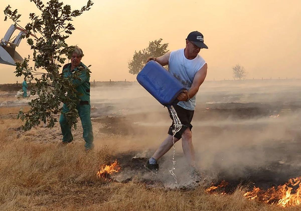 Dos personas se esfuerzan en apagar el fuego de Cipérez este viernes.