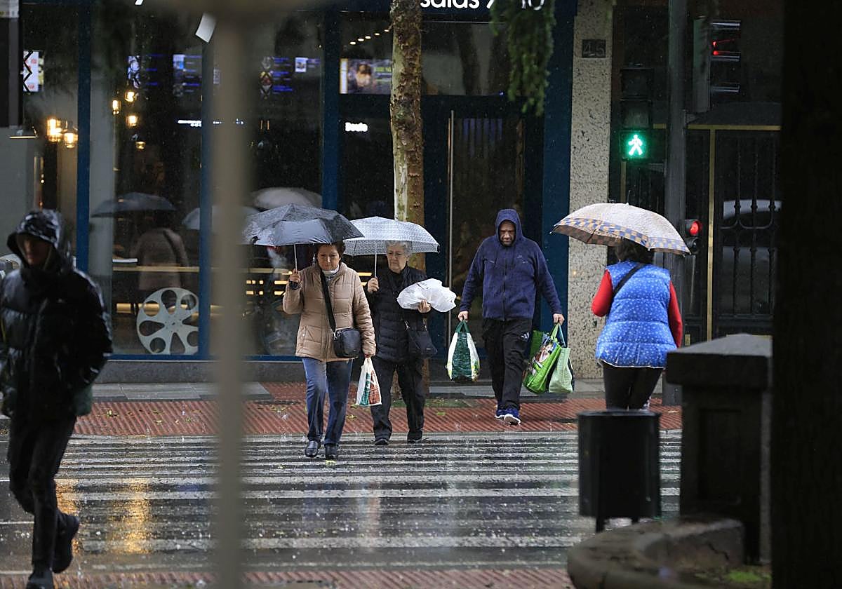 Varias personas pasan un paso de cebra protegidos con un paraguas.