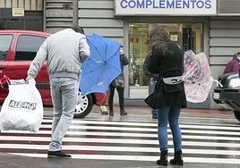 Varias personas cruzan por un paso de peatones en un día de viento y lluvia en Salamanca.