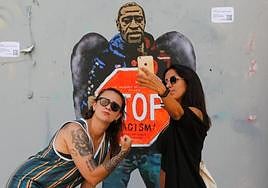 Two women stand next to a mural of George Floyd, who was killed by police in the United States.