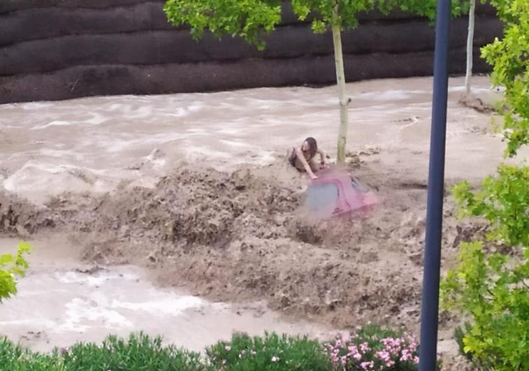 A woman clings to the roof of her vehicle to avoid being swept away by the flood.