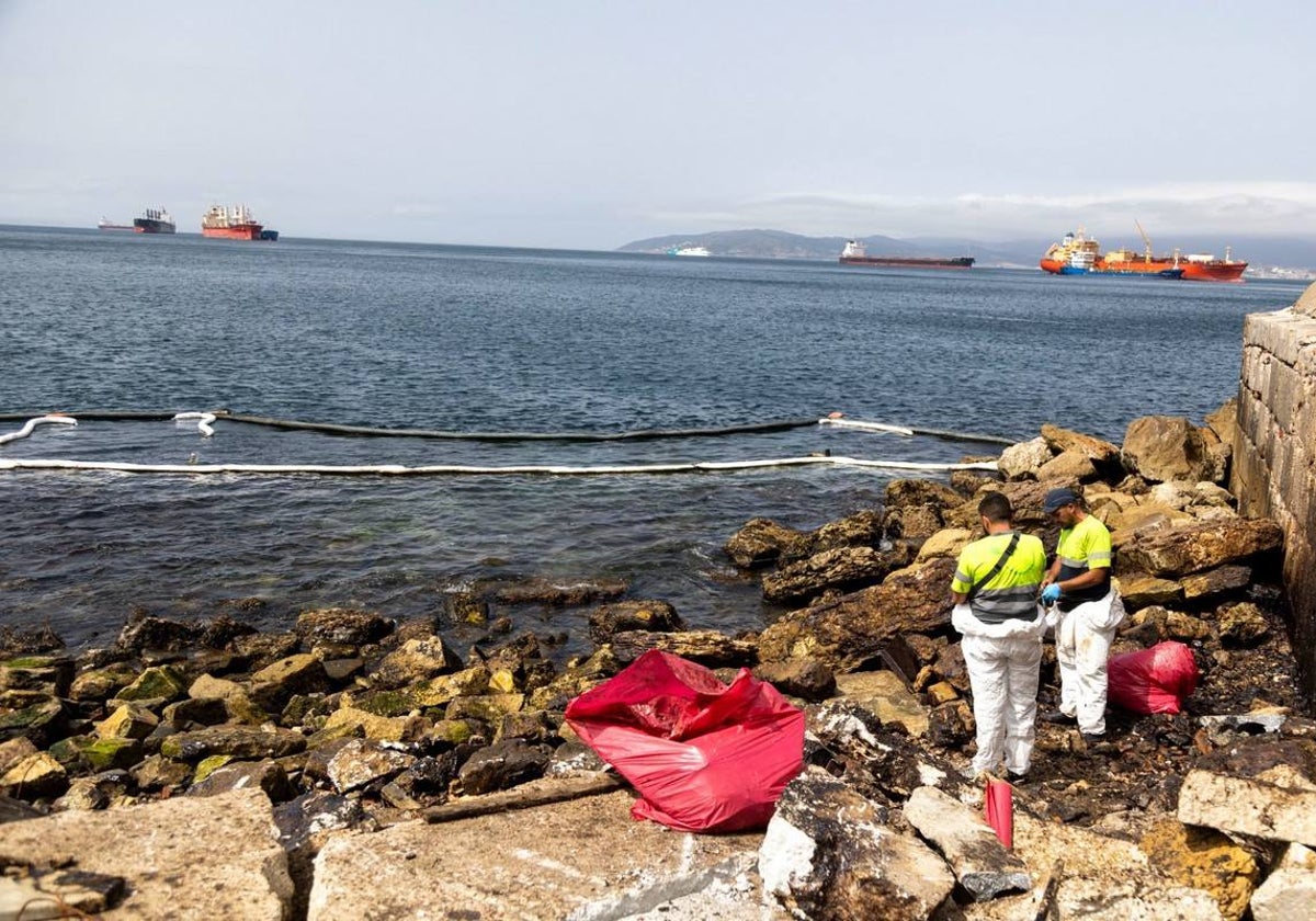 Officials at the scene of the oil spill clean contaminated rocks and rubble on the coastline