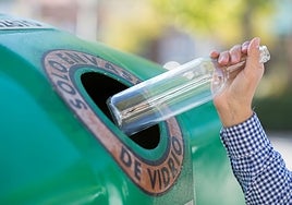 A conscientious person dropping a glass bottle into a green bottle bank.