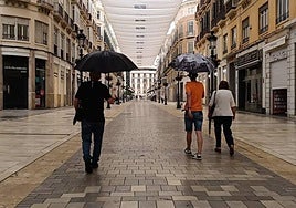 People walk under umbrellas during the last episode of rain in Calle Larios.