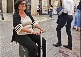 A woman moves along Calle Larios in Malaga city centre sat on top of a motorised suitcase.