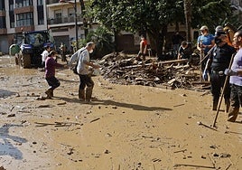 Two elderly people try to cross a street flooded by a river of mud.