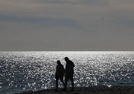 Two people stroll along the beach.