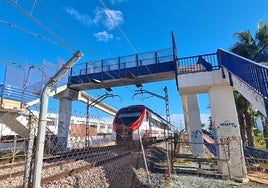 A train passes under the footbridge, which is in very bad condition.