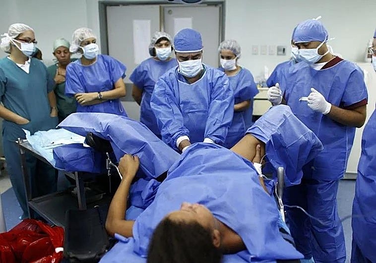 A doctor delivers a baby while a group of medical students look on.
