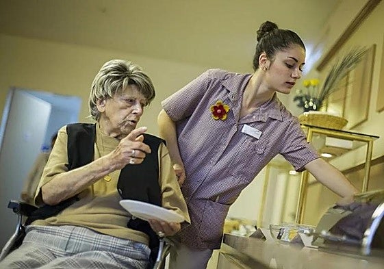 An auxiliary helps a person in a nursing home to choose the food she is going to eat.
