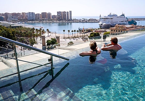 Tourists enjoy a hotel swimming pool overlooking the port in Malaga city.