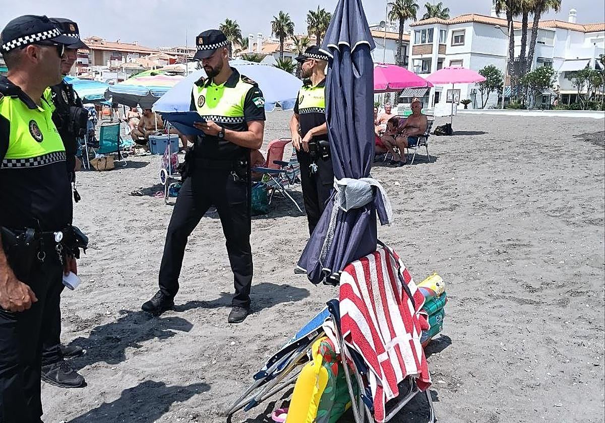 Local Police officers inspect umbrellas and chairs on a beach in Torrox Costa.