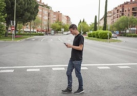 'Distracted walking': young man crosses a street with his eyes glued to his mobile phone.