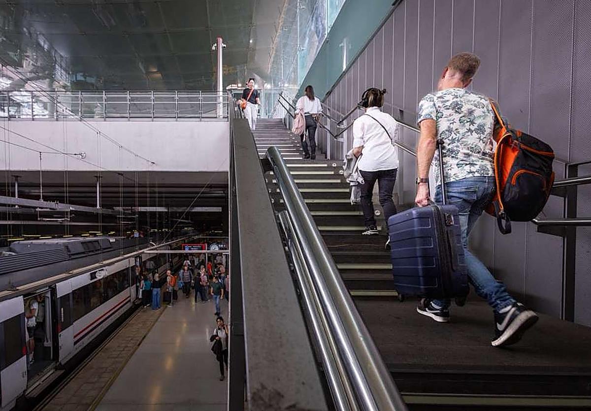 Passengers carry suitcases up the Renfe station stairs at the airport.
